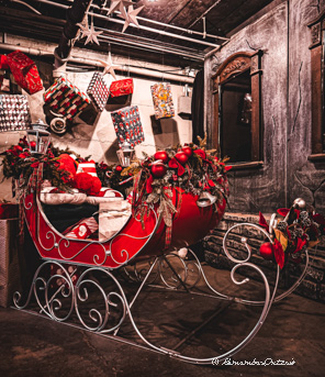 A red sled is decorated with wreaths and red Christmas ornaments.