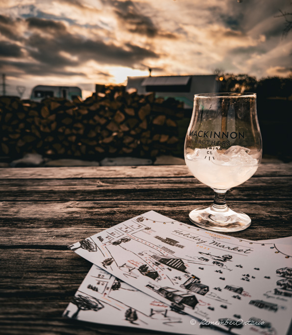 A glass of drink and two hand-drawn-map postcards is on a rustic wooden table during the sunset.