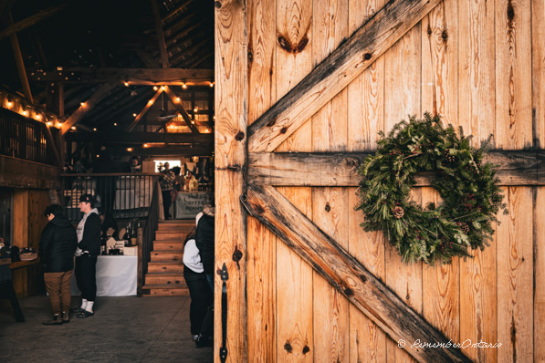 Peek through Half-open wooden barn door decorated by Christmas wreath to see people shopping inside.